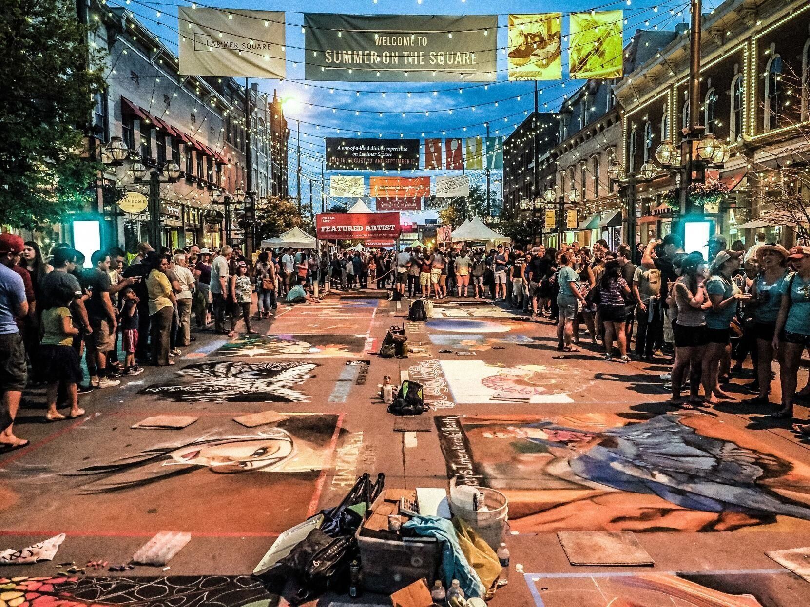 Una calle con tiendas de campaña y gente reunida, pancartas colgando y obras de arte en el suelo.