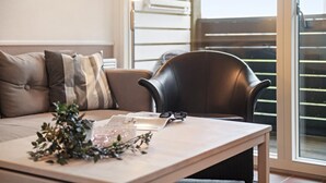 Un salon moderne avec un canapé, un fauteuil, une table agrémentée d’objets décoratifs et une vue sur un balcon.