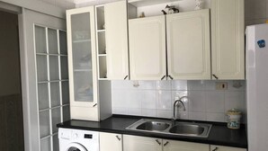 Una cocina compacta con armarios blancos, lavadora, pileta y refrigerador.