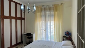 Un dormitorio con cama, escritorio, silla, ventilador y ventana con cortinas.