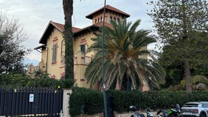 Un edificio con una torre característica y una entrada protegida por una reja.