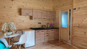 Een compact houten vakantiehuisje met een kitchenette, een eethoek met tafel en stoelen, en een kleine koelkast.