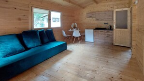 Een houten hut met een blauwe bank, een eettafel met stoelen en een kitchenette.