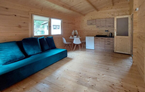 L’intérieur d’une cabane en bois, avec un canapé bleu, une petite table à manger et des chaises, ainsi qu’un coin cuisine.