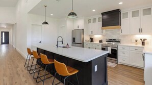 A modern kitchen with a large island, bar stools, stainless steel appliances, and white cabinetry. - Spacious family/group stay near downtown (McKinney)