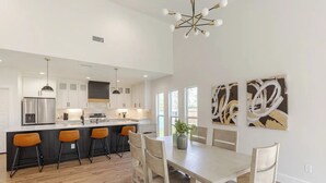A modern kitchen with a central island, bar stools, and a dining table with chairs. - Spacious family/group stay near downtown (McKinney)
