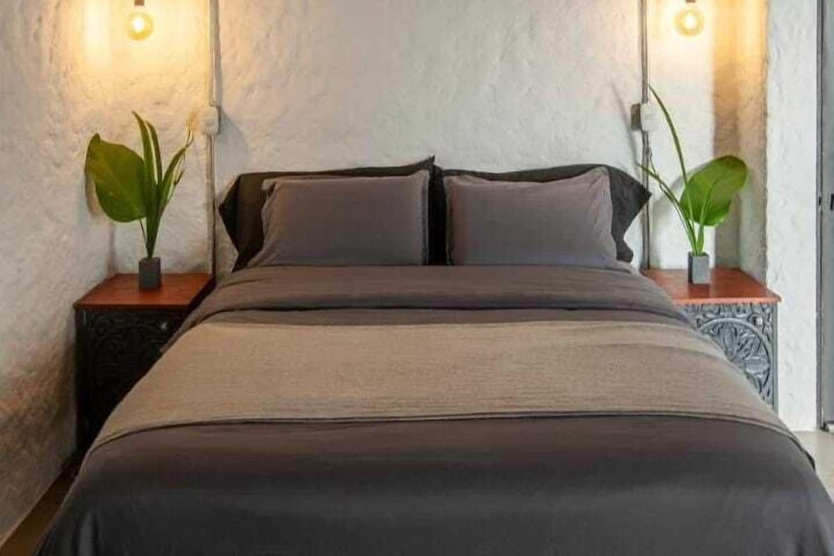 A bedroom with a wooden ceiling, two bedside tables with lamps, and a bed with a dark-colored bedspread.