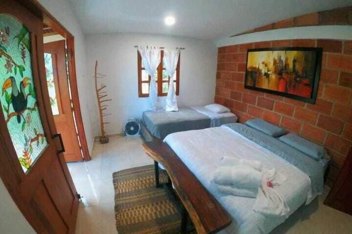 A bedroom with two single beds, a bench, a radiator, a window with curtains, and a painting on the wall.