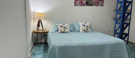 Un dormitorio con una cama, una mesita de noche, una lámpara, un cuadro y una escalera metálica azul.