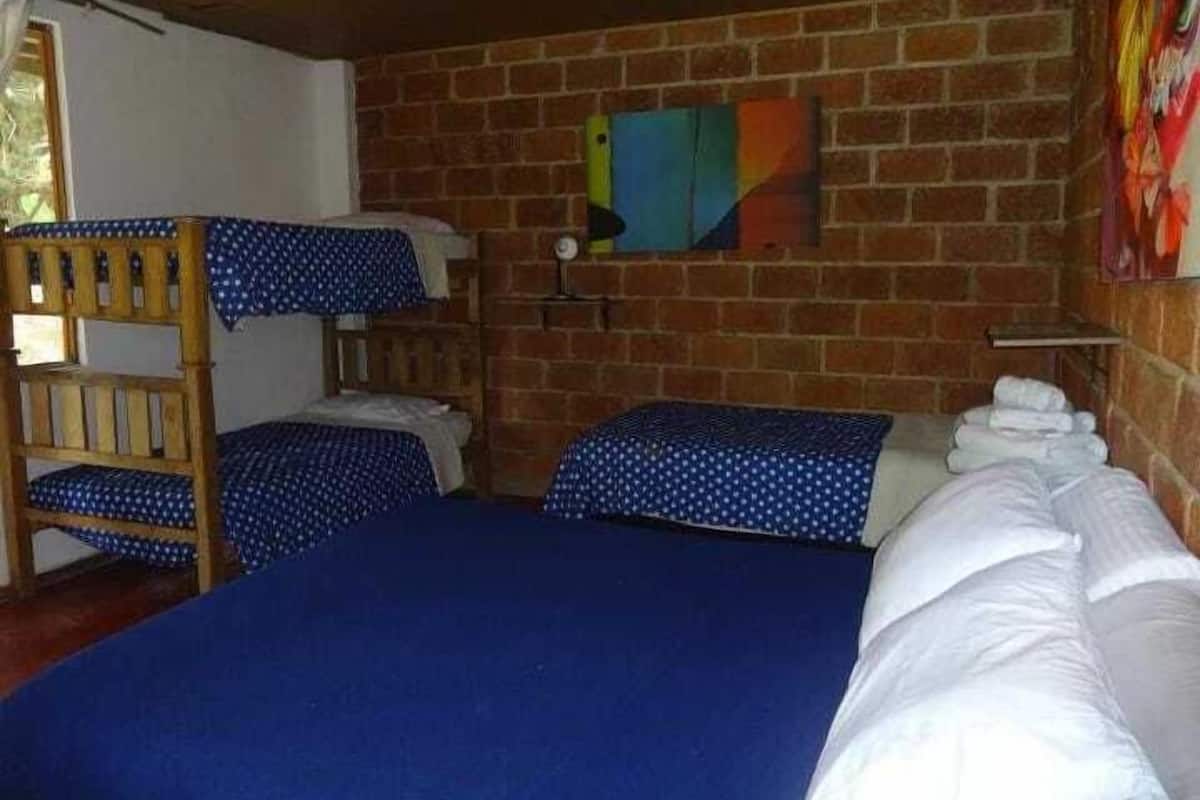A room with a brick wall, two bunk beds with blue bedding, a wooden chair, and a small shelf with towels.