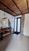 Un baño con techo de madera, un espejo grande, un lavabo con pileta negra y una pared de piedra.