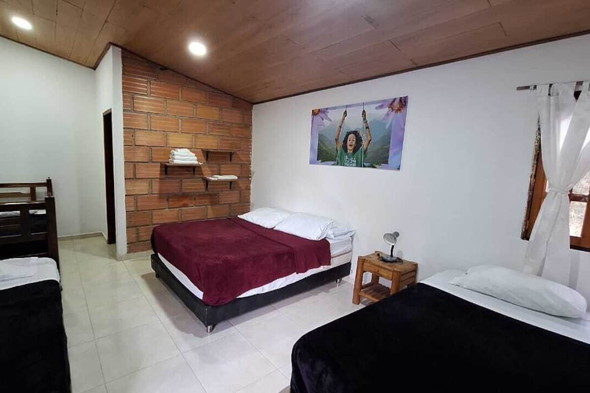 A bedroom with two beds, a brick accent wall, a wooden ceiling, and a small bedside table with a lamp.