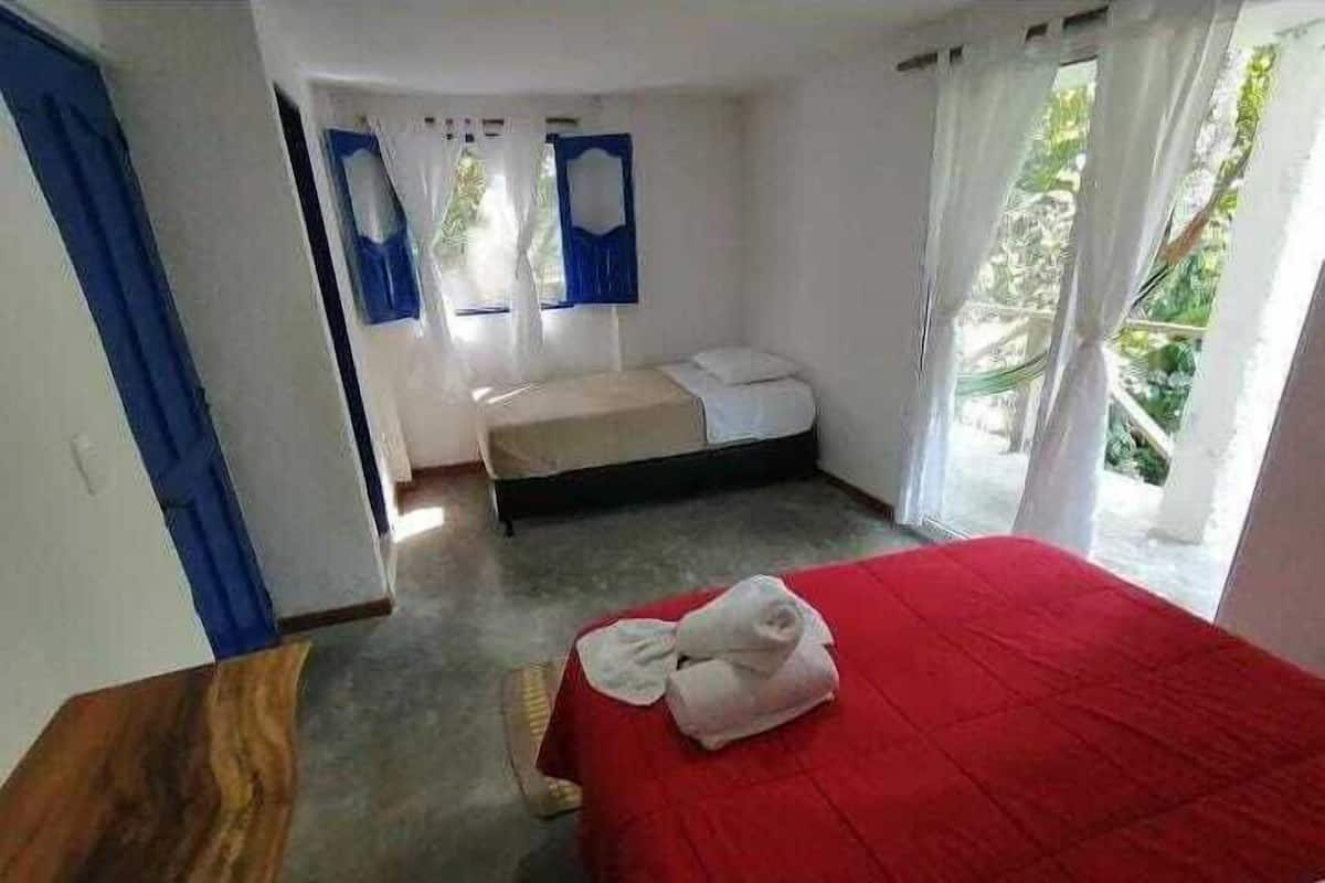 A bedroom with a red bedspread, a wooden nightstand, a single bed, and a window with curtains.