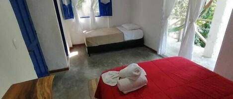 Un dormitorio con una colcha roja, una mesita de noche de madera, una cama individual y una ventana con cortinas.