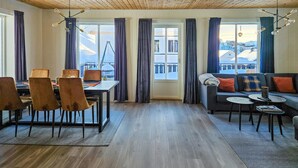 Sala de estar moderna com área de jantar, piso de madeira e grandes janelas com cortinas.
