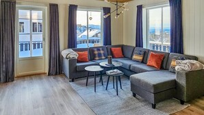 Uma sala de estar moderna com um sofá modular cinzento, duas mesas de centro redondas e vista para uma paisagem nevada através de grandes janelas.