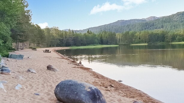 Uma praia à beira de um lago, com uma mesa para piquenique e pedras.