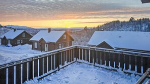 Um bairro residencial com casas cobertas de neve, uma cerca de madeira e um pôr do sol ao fundo.