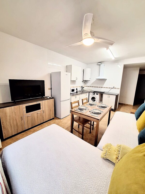 Un espacio habitable compacto con kitchenette, zona de comedor y sala de estar con sofá y cama.
