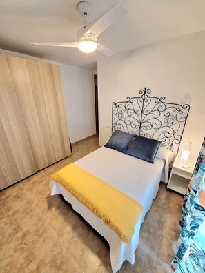 Un dormitorio con cama, ventilador de techo, mesita de noche y lámpara de pared.