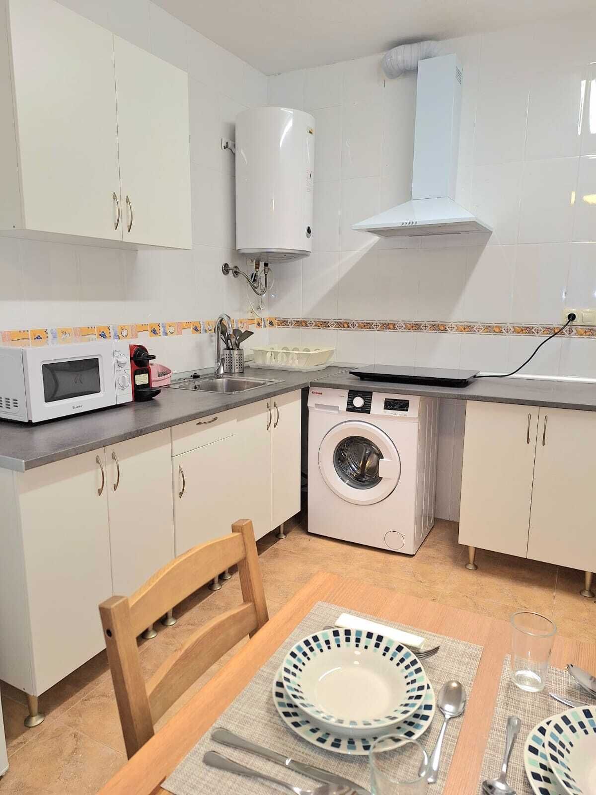 A compact kitchen with white cabinets, a microwave, a washing machine, and a sink.