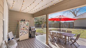 Eine überdachte Terrasse mit Grill, Tisch und Stühlen im Freien sowie Lichterketten.