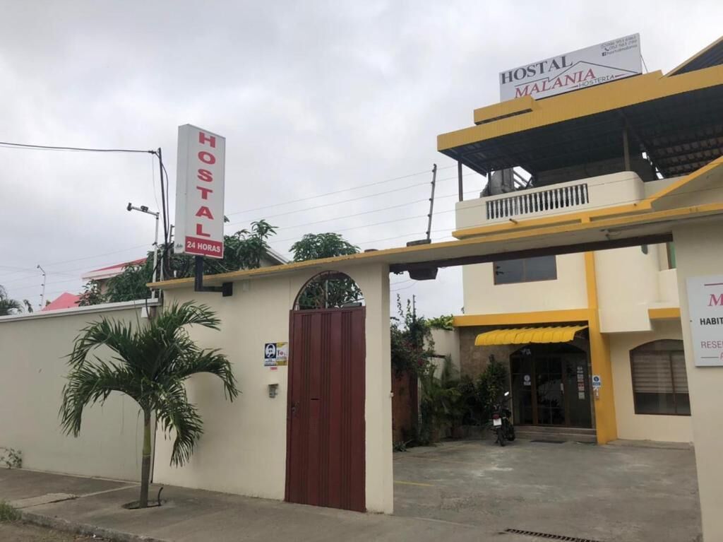 Un hostal llamado "Hostal Malania" con un letrero de servicio las 24 horas, una entrada con portón y un balcón visible.