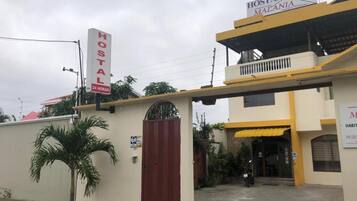 Un hostal llamado "Hostal Malania" con un letrero de servicio las 24 horas, una entrada con portón y un balcón visible.