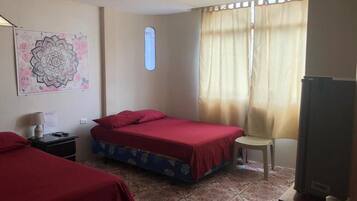 Una habitación con dos camas, una silla, un ventanal con cortinas, un adorno en la pared y un televisor.