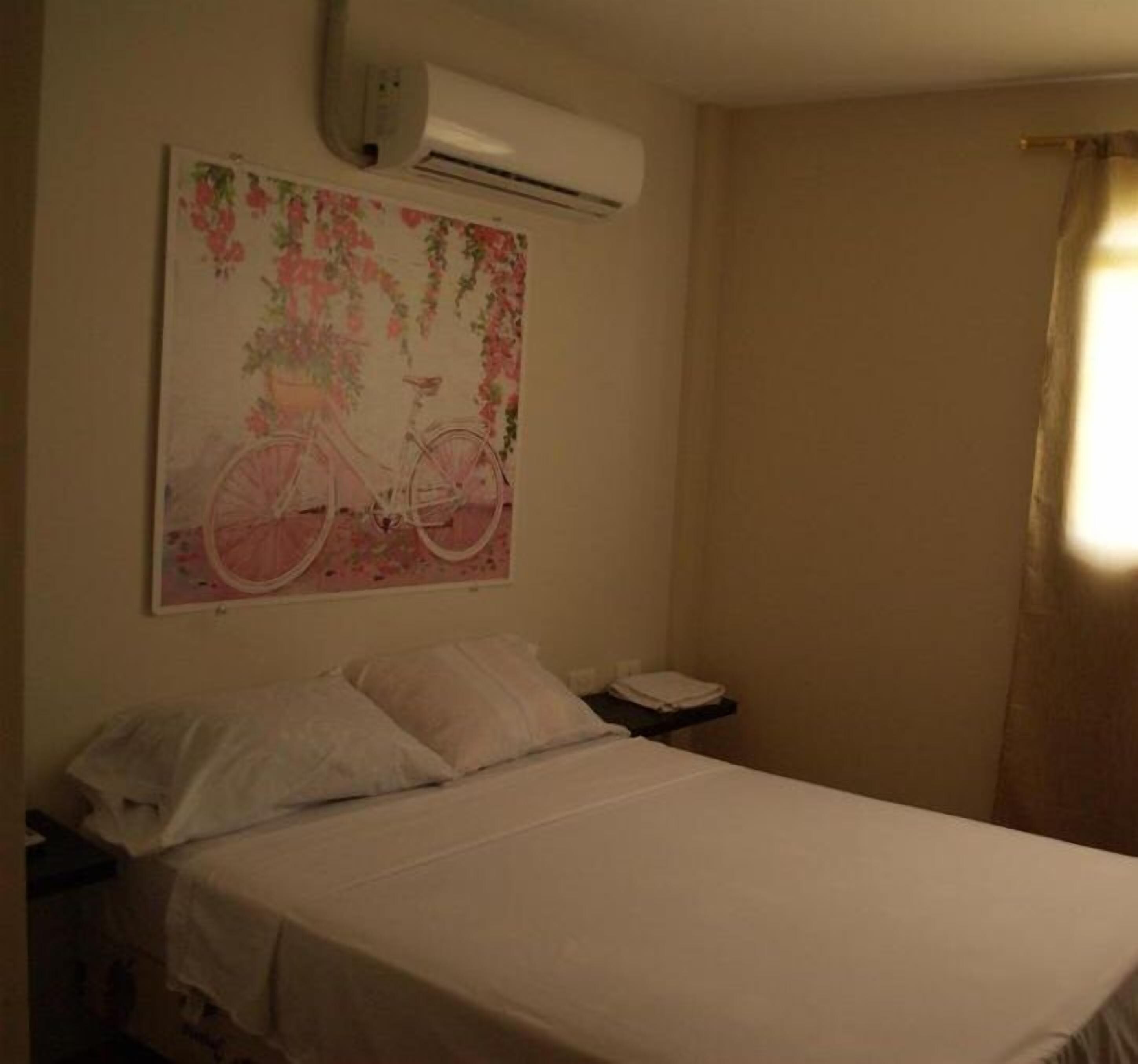 Een slaapkamer met een bed, nachtkastje, airconditioning en een bloemrijk schilderij aan de muur.