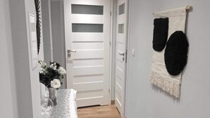 A narrow hallway with a wooden floor, a black rug, a white door with horizontal stripes, and a wall-mounted decorative item. - Stunning, remodeled condo in historic building along Odra River! (Szczecin)