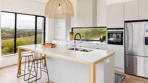 Een moderne keuken met een groot schiereiland, roestvrijstalen apparatuur en uitzicht op een groen landschap.