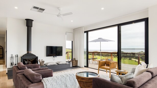 Een moderne woonkamer met een open haard, comfortabele zithoek, een flatscreen-tv en een grote glazen schuindeur die leidt naar een terras.