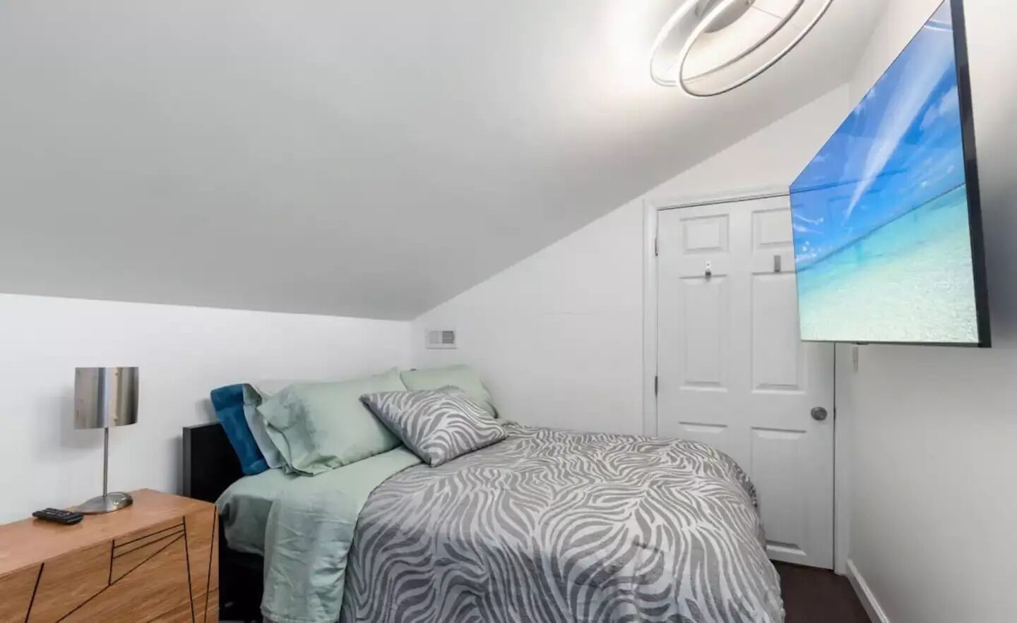 A bedroom with a bed, a nightstand, a lamp, and a door.