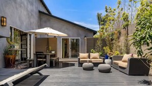 Een modern terras buiten met een houten dek, een zithoek en een eethoek.
