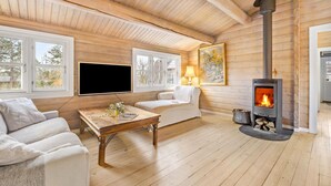 Ein gemütliches Blockhäuschen-Interieur mit Kamin, Holzwänden, einer Couch, einem Fernseher und einem Tisch.