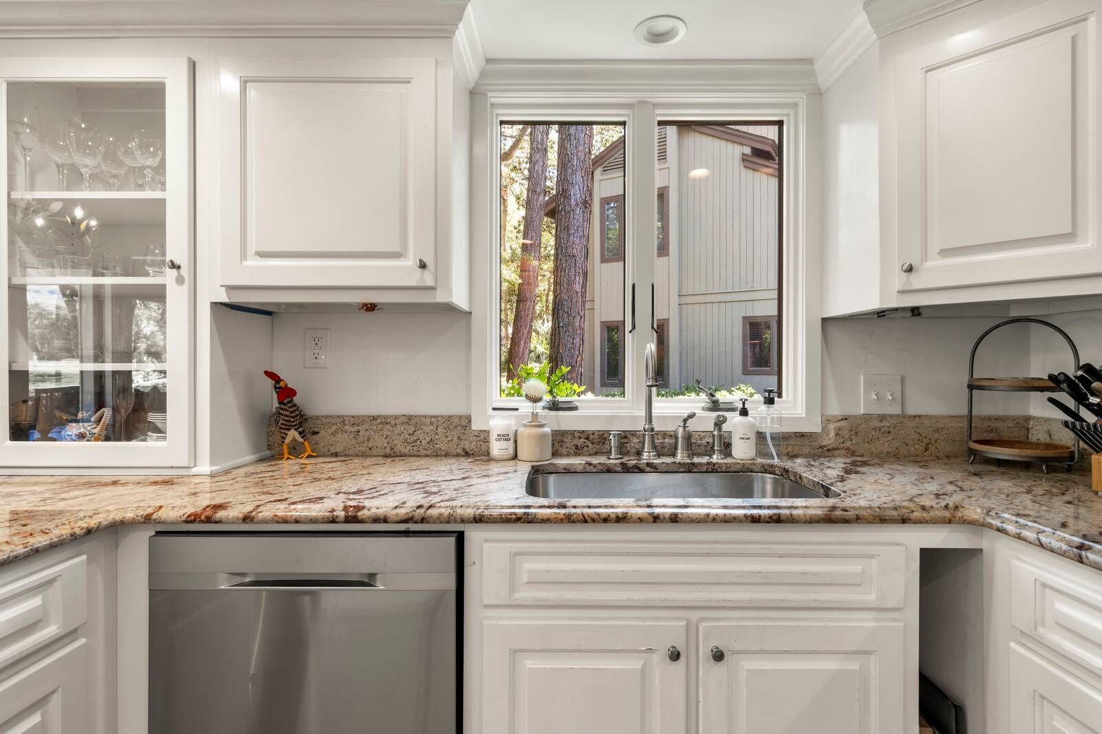 A kitchen with white cabinets, a granite countertop, a stainless steel sink, and a dishwasher.