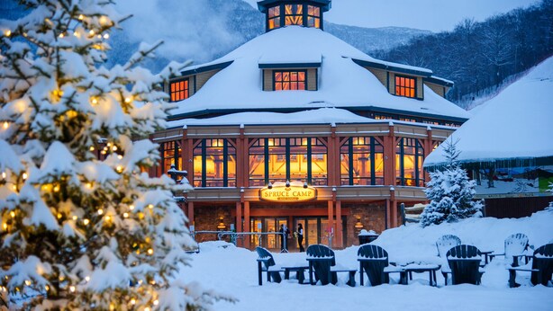 A snow-covered lodge with a prominent sign reading "Spruce Camp Base Lodge." - #1315 | STUDIO | The Lodge At Spruce Peak | Big Mountain Views 3rd floor (Stowe)