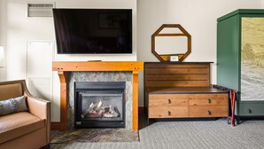 A living room with a fireplace, a television mounted on the wall, and a green cabinet with a painting. - #1315 | STUDIO | The Lodge At Spruce Peak | Big Mountain Views 3rd floor (Stowe)