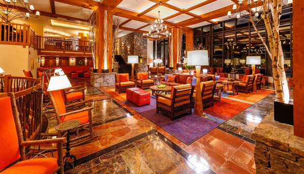 A spacious lobby with a stone fireplace, wooden furniture, and a large chandelier.