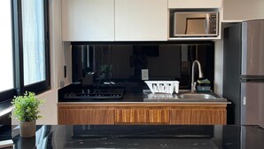 A modern kitchen with a black countertop, stainless steel appliances, and wooden cabinetry. - DOI 45 Apartment (Playa del Carmen)