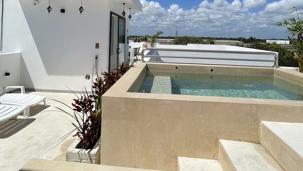 A modern outdoor pool area with a white building, clear blue sky, and a view of the cityscape. - DOI 45 Apartment (Playa del Carmen)