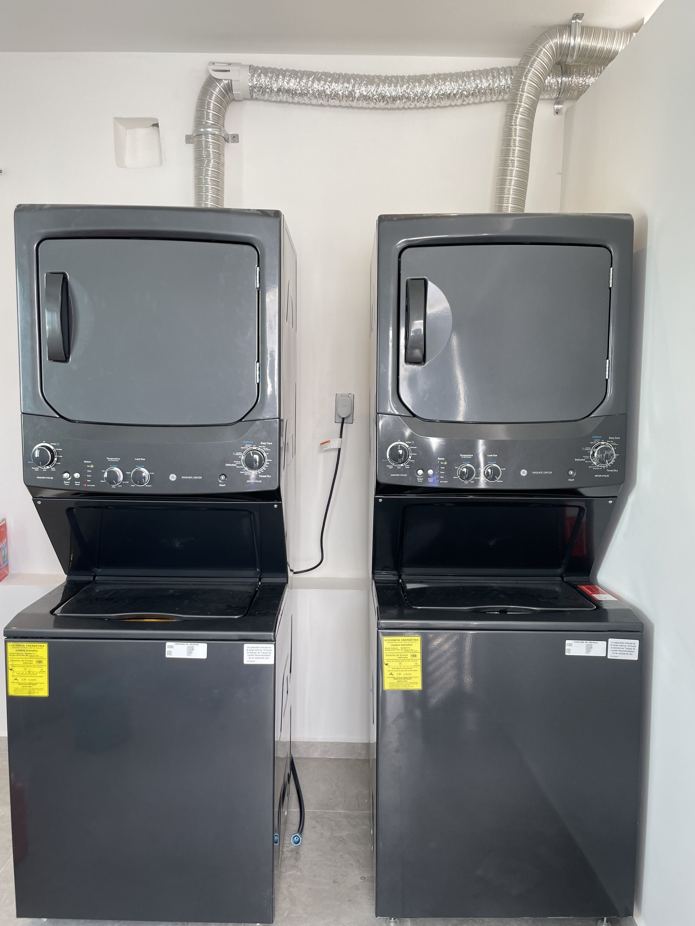 Two stacked washing machines with control panels, a power outlet, and a vent pipe above.