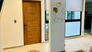 A hallway with a wooden door, a large window, and a modern art piece on the wall. - DOI 45 Apartment (Playa del Carmen)