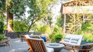 Terraza al aire libre con mobiliario de madera, incluyendo sillas y una mesa, rodeada de abundante vegetación y árboles.