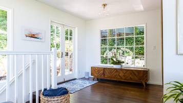 Una habitación luminosa con suelo de madera, barandilla blanca, un armario de madera y un ventanal con vistas a la vegetación.