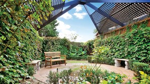 A garden with a wooden bench and a stone planter. - Buckingham Apartment (Highett)