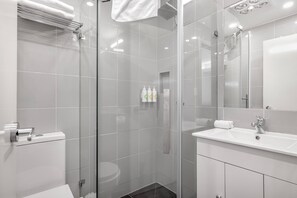 A modern bathroom with a glass shower enclosure, a white sink, and a large mirror. - Buckingham Apartment (Highett)