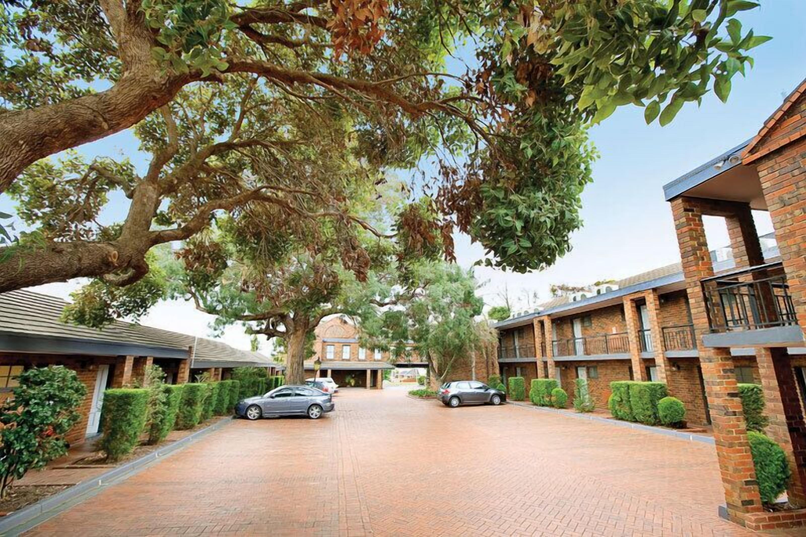 A brick building with a central courtyard, surrounded by hedges and trees.