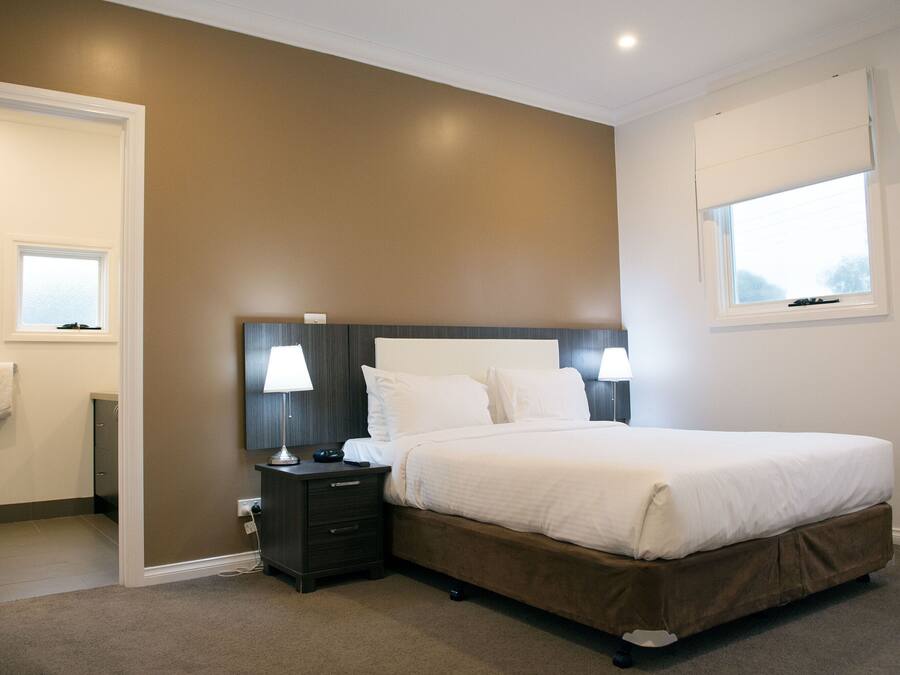 A bedroom with a large bed, two bedside lamps, a nightstand, and a window with a view.
